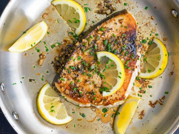 A pan-fried swordfish steak garnished with lemon wedges and chives