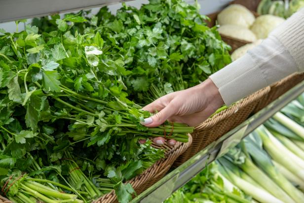 A woman takes a bunch of fresh green parsley from the supermarket