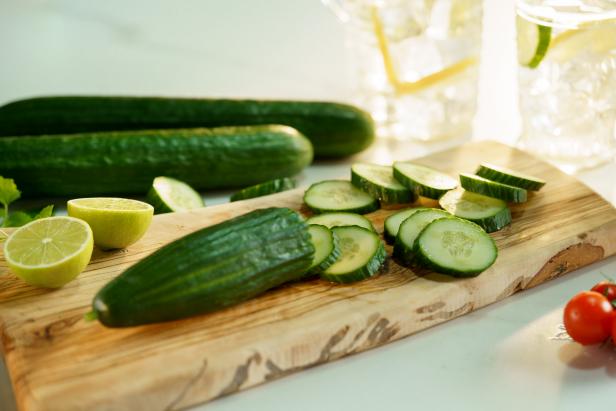 High angle of cut ripe cucumber and halved lime on wooden chopping board near lemonade with ice cubes and cherry tomatoes
