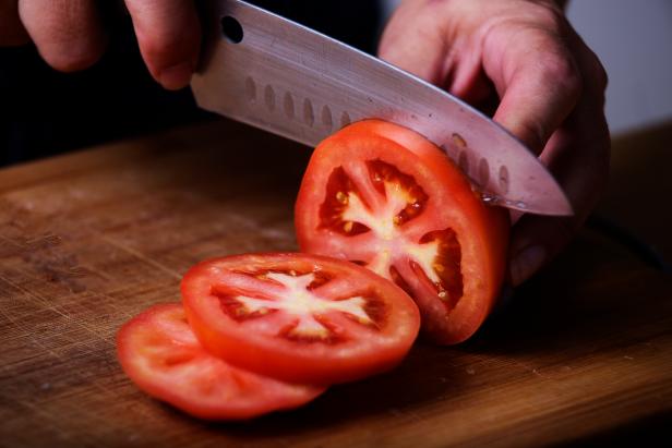 Tomato being sliced with a sharp kitchen knife