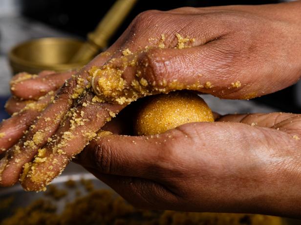 Besan-sooji ladoo (sweet balls made of gram-flour/chickpea-flour) being shaped by hand in traditional Indian style