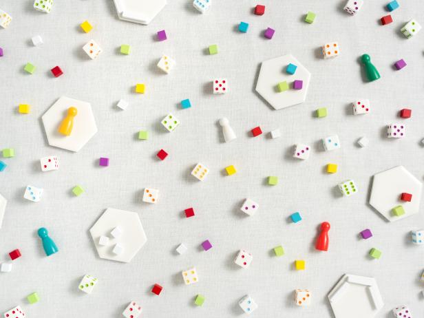 Horizontal, full frame image of brightly colored , modern game pieces scattered randomly on a white background. The game pieces include meeples, hexagonal tiles, dice, and cubes.