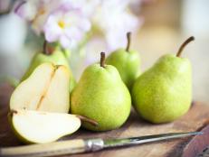 Green pears on wooden board with knife.