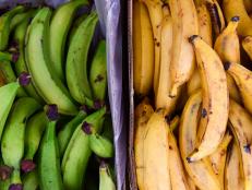 Close up overhead view of two piles of green and yellow plantains on sale at a market in London