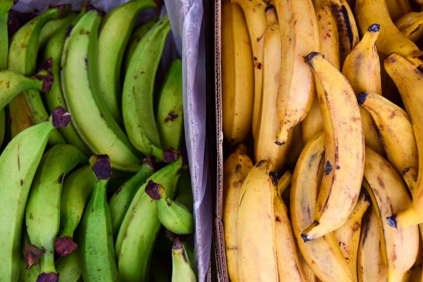 Close up overhead view of two piles of green and yellow plantains on sale at a market in London