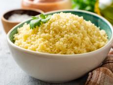 Cooked couscous with cilantro in ceramic bowl on concrete background. Selective focus.
