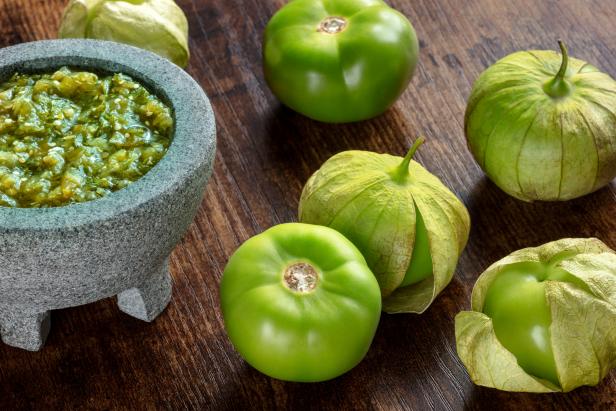 Tomatillos, green tomatoes, with salsa verde, green sauce, in a molcajete, traditional Mexican mortar, on a dark rustic wooden background