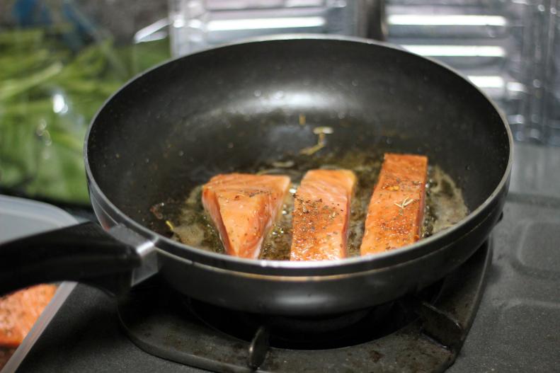 picture of 3 pieces of salmon cooking in a pan with butter