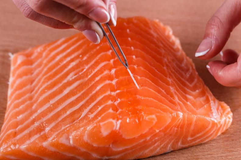 young woman removes bones from a salmon fillet.