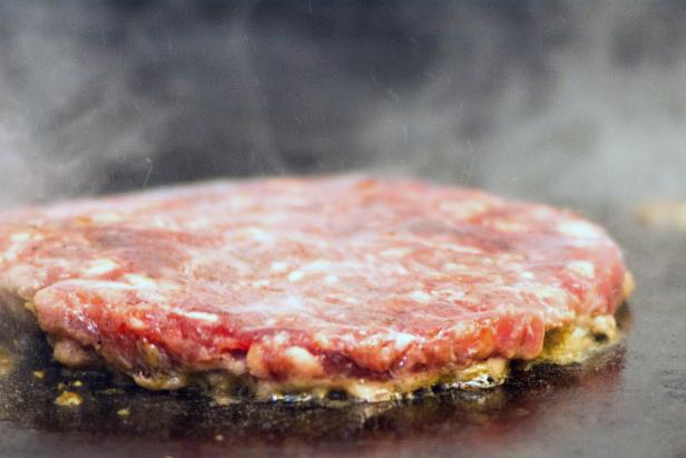 Hamburger meat medallion is cooked on iron