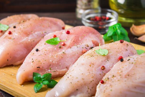 874059338 Raw chicken fillets on a cutting board against the background of a wooden table. Meat ingredients for cooking