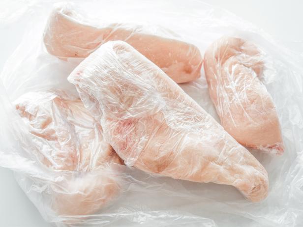 1770449425 Frozen chicken breast in food plastic wrap or cling film. Photo can be used for how to wrap meat for freezer concept.