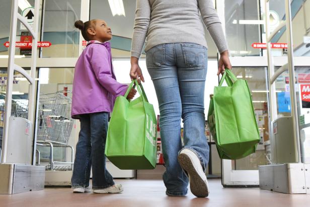 A mom and her four-year-old daughter walk out of grocery store holding their reusable grocery bags.