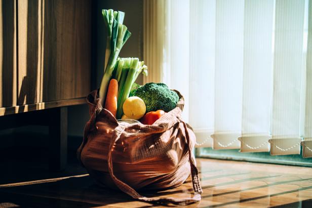 Eco-friendly reusable shopping bag with multi-coloured fresh organic fruits and vegetables at home. Shopping with reusable grocery bag for plastic free and waste-free life. Responsible shopping. Zero waste food shopping and sustainable lifestyle concept