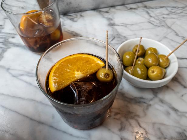 Black vermouth with orange and ice served with stuffed olives
