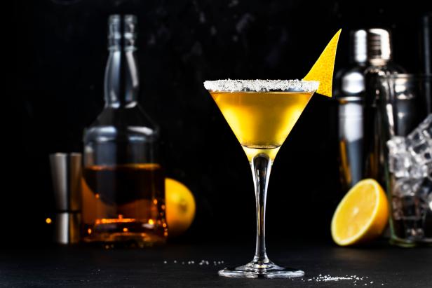 Sidecar classic alcoholic cocktail with cognac, liqueur, lemon juice and ice. Black background, bar tools, night atmosphere