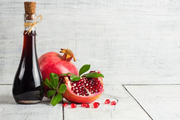 Glass bottle of pomegranate sour sauce with fresh ripe whole and split pomegranate fruit with leave on rustic background