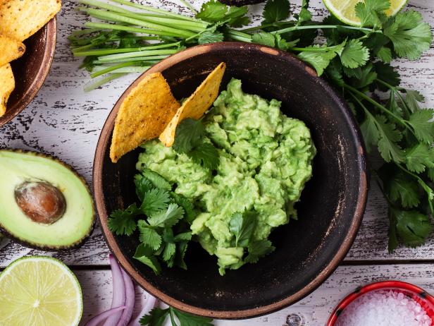 1199747658 Making guacamole sauce, avocado, cilantro, lime, pepper, salt, tortilla corn chips. Mexican cuisine ingredients on rustic wooden background, top view