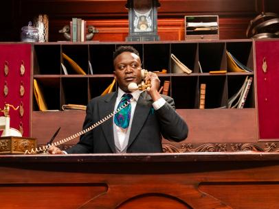 Host Tituss Burgess at the front desk, as seen on Last Bite Hotel, Season 1.
