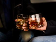 Two hands clink glasses of whiskey wiskey on the couch, cozy. Bar drinking menu.