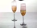 A unique and different drink is being poured into two glasses. These glasses hold a champagne cocktail that is good for you and contains an infusion of ginger and candied ginger.