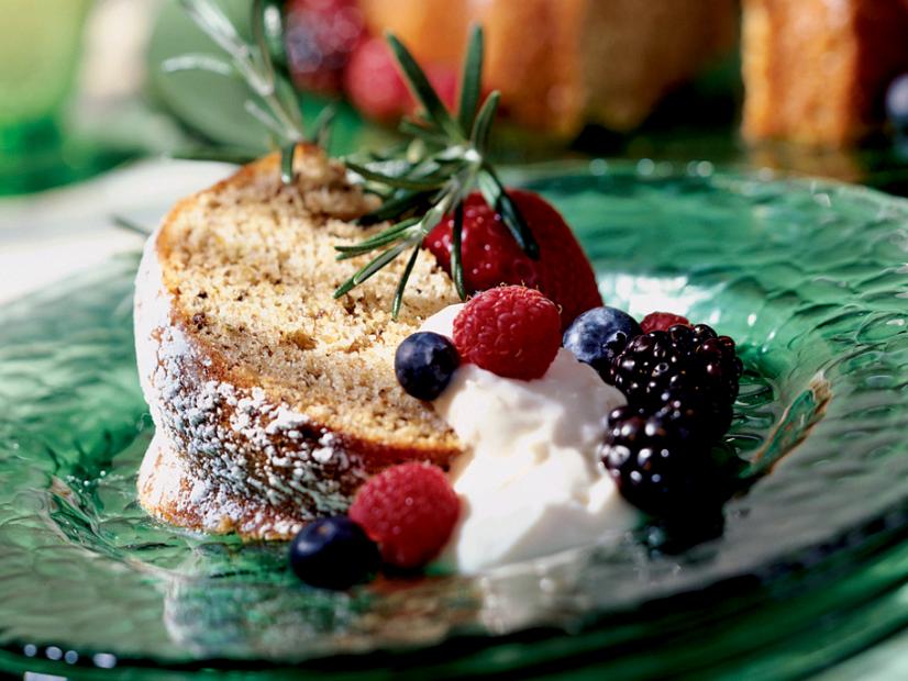 A Slice of Walnut Cake Rosemary with a Dollop of Cream and Various Berries on a Decorative Green Glass Plate