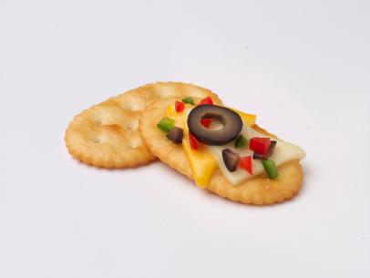 Two TownHouse Crackers Against a White Background.  One of Which Has Cheesy Southwest Appetizer Ingredients on It.