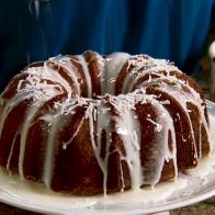 Bundt Cake with Pineapple Glaze and Sprinkled Coconut Flakes on Top a White Cake Pedestal