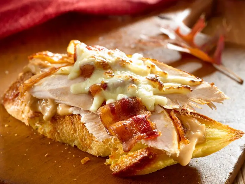 A BBQ Turkey Sandwich Topped with Bacon and Cheese on a Block of Wood