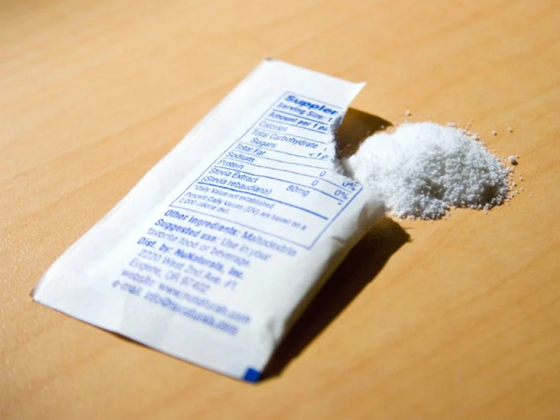 A Torn Packet of Artifical Sweetener Facedown on a Wood-like Surface