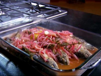 A glass cooking dish with four whole trouts covered in julienned red onions, Thyme Sprigs and lemon zest