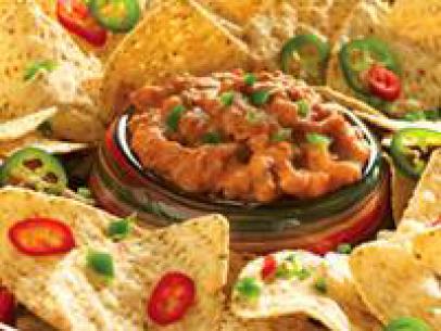 A Platter filled with Nachos topped with sliced peppers with dip in the center