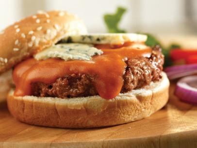 A Buffalo Burger topped with sauce and slices of blue cheese while placed on a wooden block 