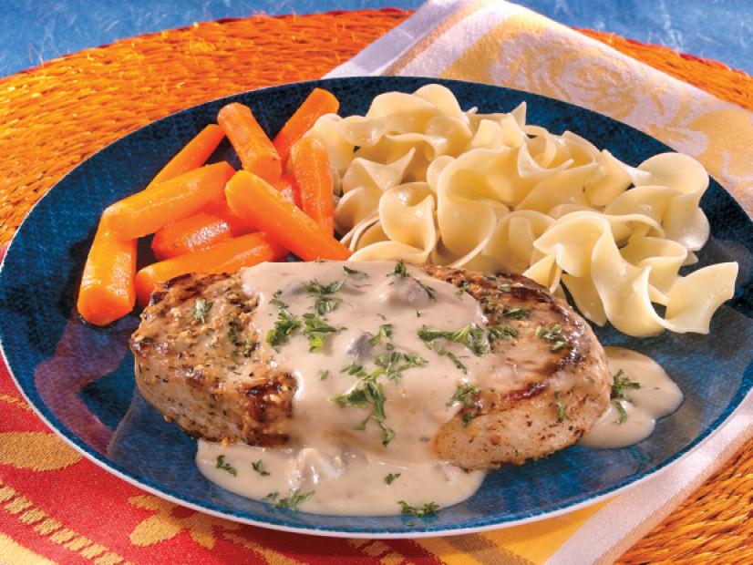 Creamy Mustard Pork Chop on a dark blue plate with noodles and  carrots