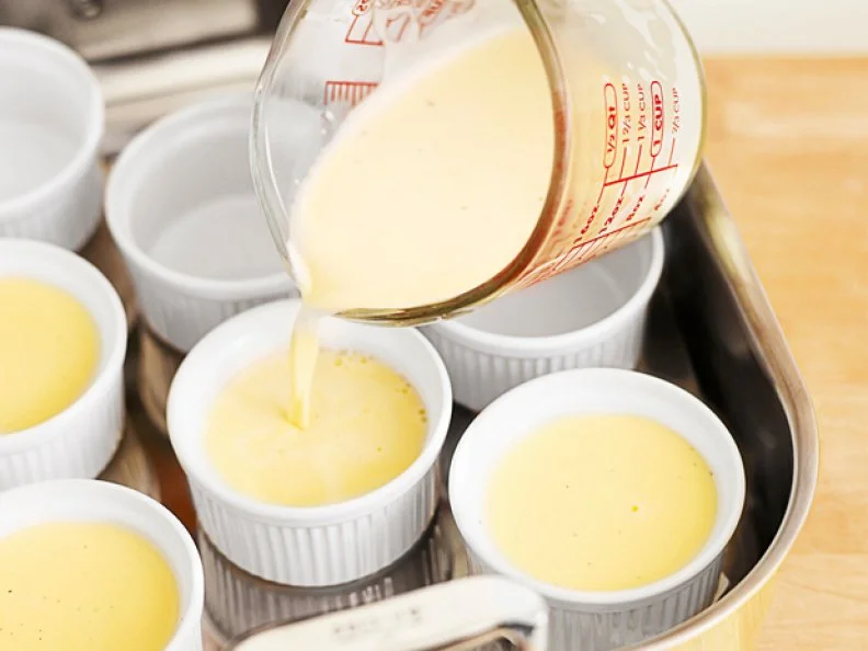 Pouring creme from a measuring cup into dishes to make creme brulee