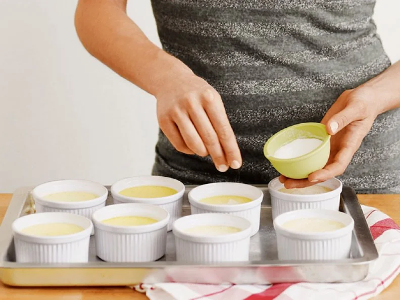 Adding ingredients to miniature dishes of creme brulee on a cooking sheet