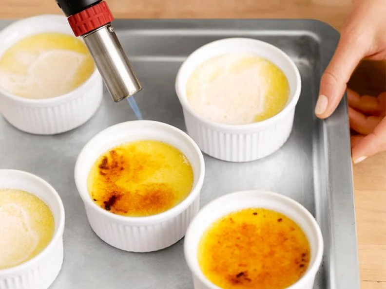 Small dishes of creme brulee being heated while on a cooking sheet