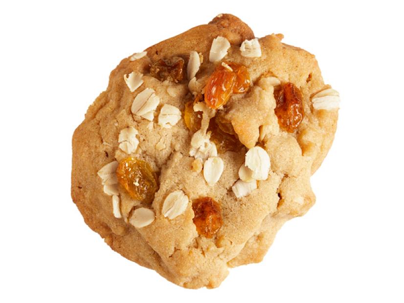 A cookie topped with golden raisins and oats placed against a white background
