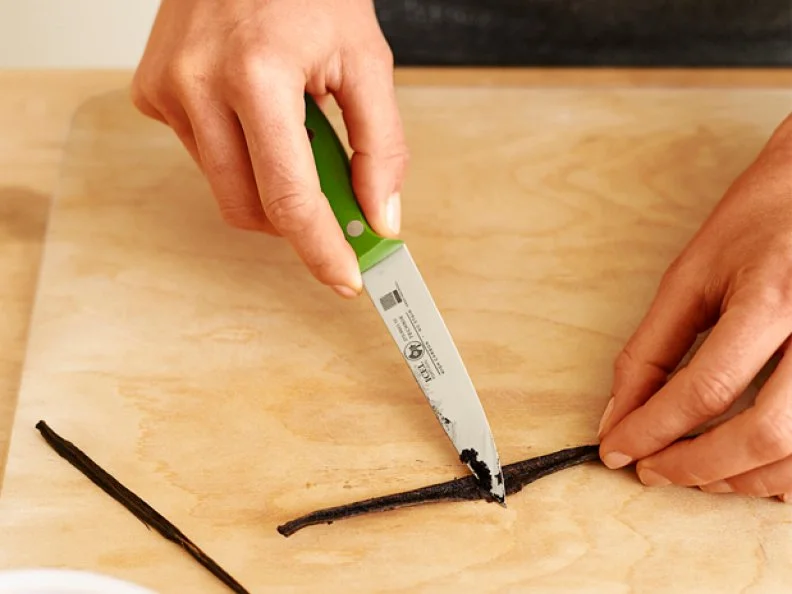 Vanilla seeds being scraped from a vanilla bean with a knife