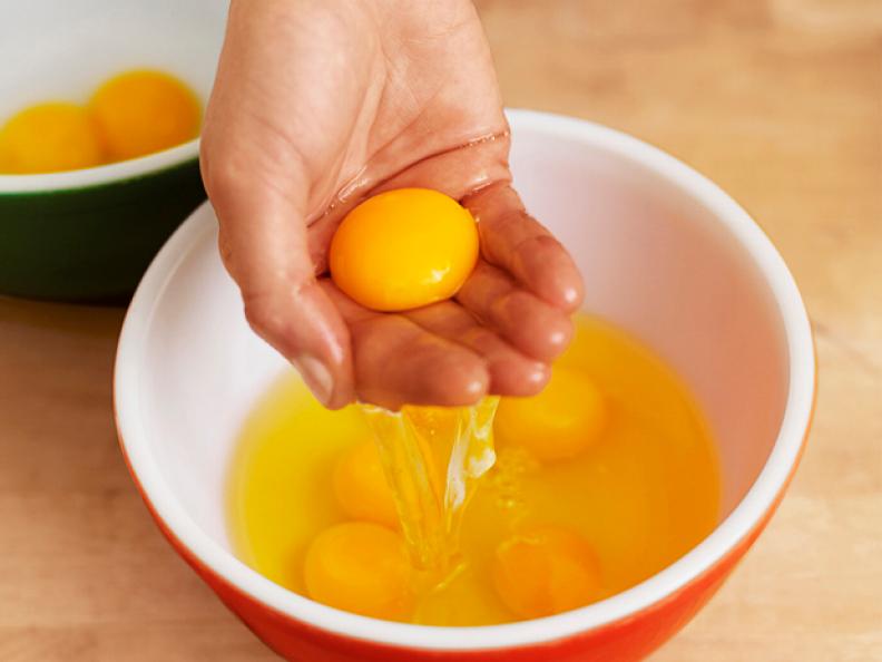A Hand Holding an Egg Yolk Scooped From Several Eggs in a Mixing Bowl 