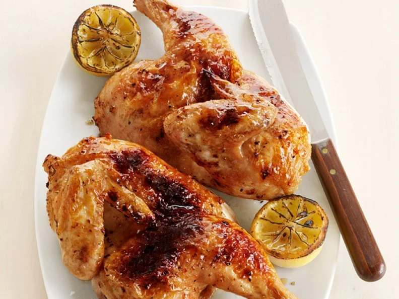 Two Pieces of Split Lemon Chicken with Cooked Lemon Halves on a Plain white Plate