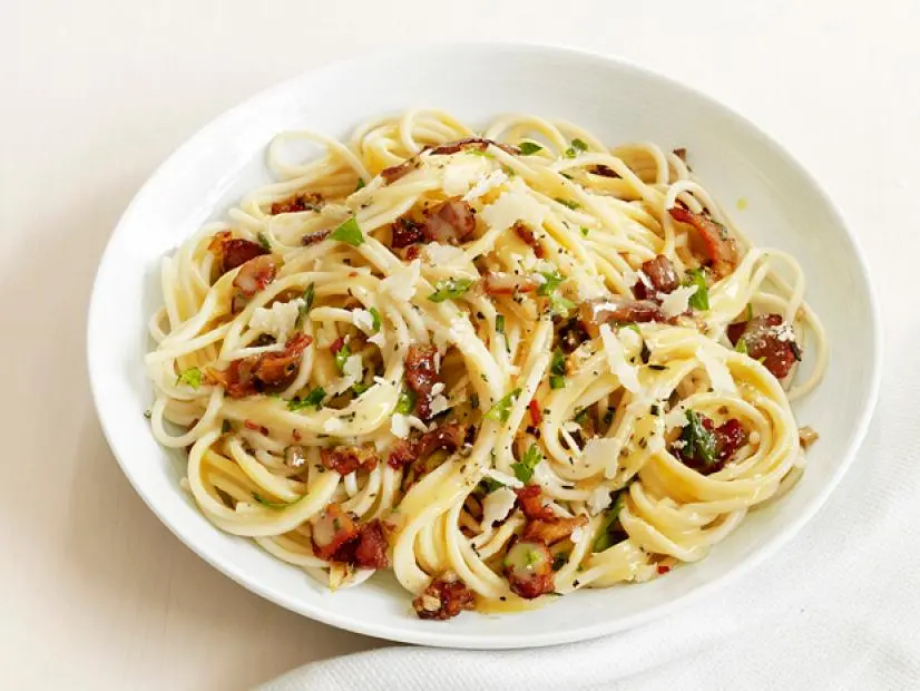 Spaghetti Carbonara sprinkled with herbs, cheese and black pepper in a white bowl on a plain white table setting