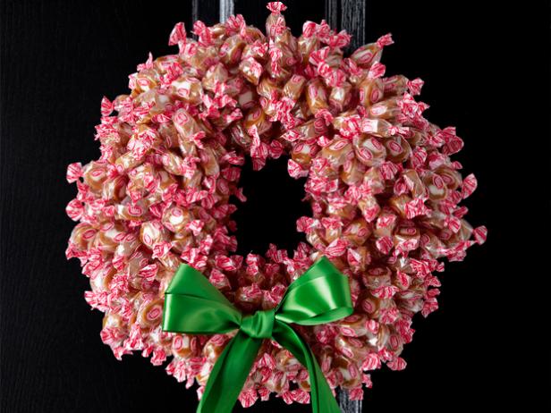 A wreath made of caramel candies with an attached green ribbon on a black door
