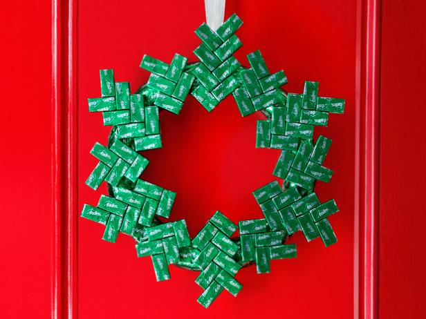 A wreath made of chocolate mints hung with silver ribbon on a red door