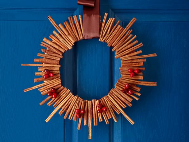 A wreath made of varying sizes of cinnamon sticks and cranberries hung with a large wine colored ribbon on a blue door
