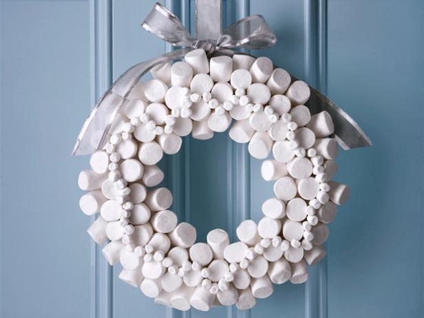 A wreath made of small and large marshmallows hung with a silver ribbon on a light blue door
