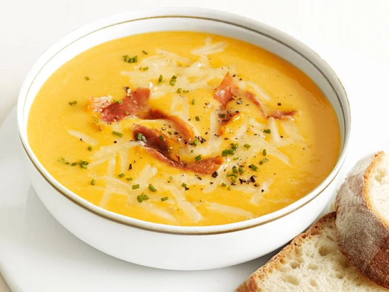 Yellow soup topped with shredded cheese, herbs, bacon and cracked black pepper
