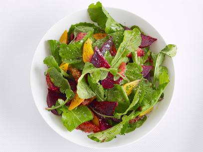 Salad made of oranges, beets and greens in a plain white bowl