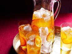 An Orange Drink with Orange slices and ice in a glass pitcher and four glasses
