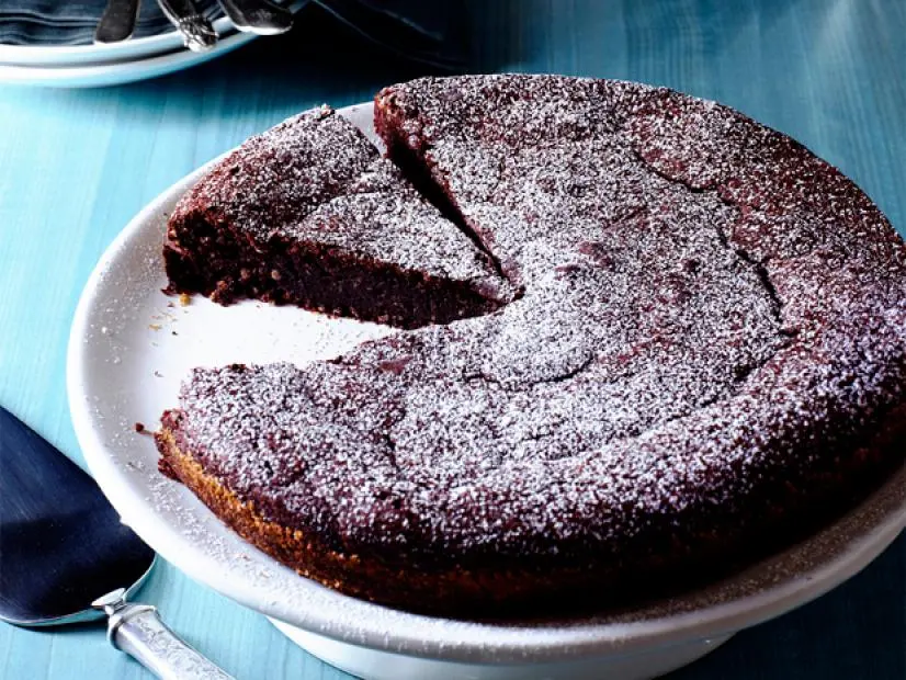 A Chocolate cake covered with powdered sugar and missing a slice 